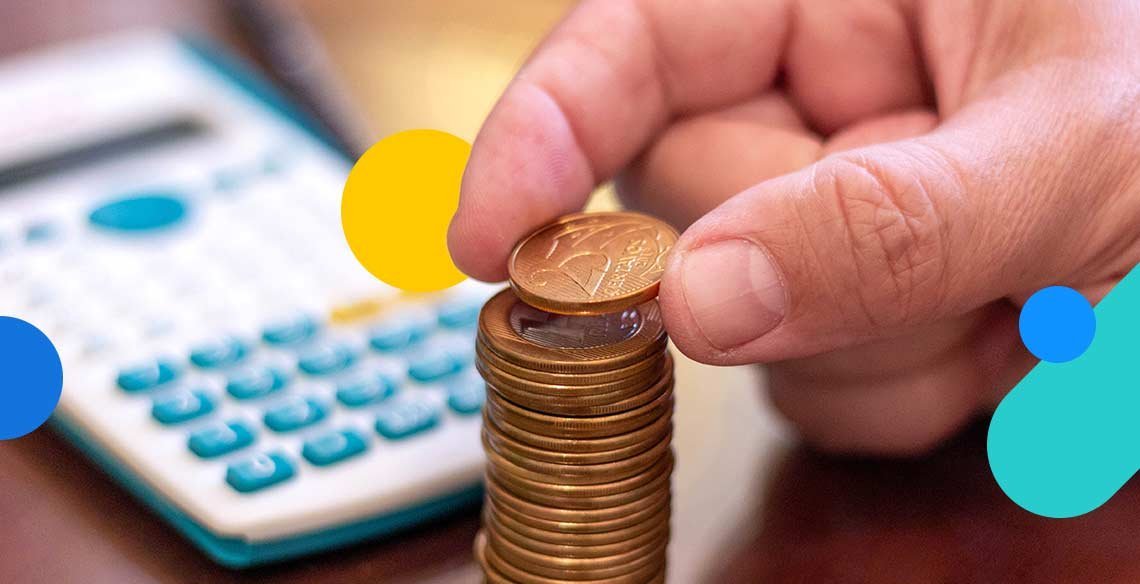 Mão colocando moeda em pilha de moedas com calculadora ao fundo