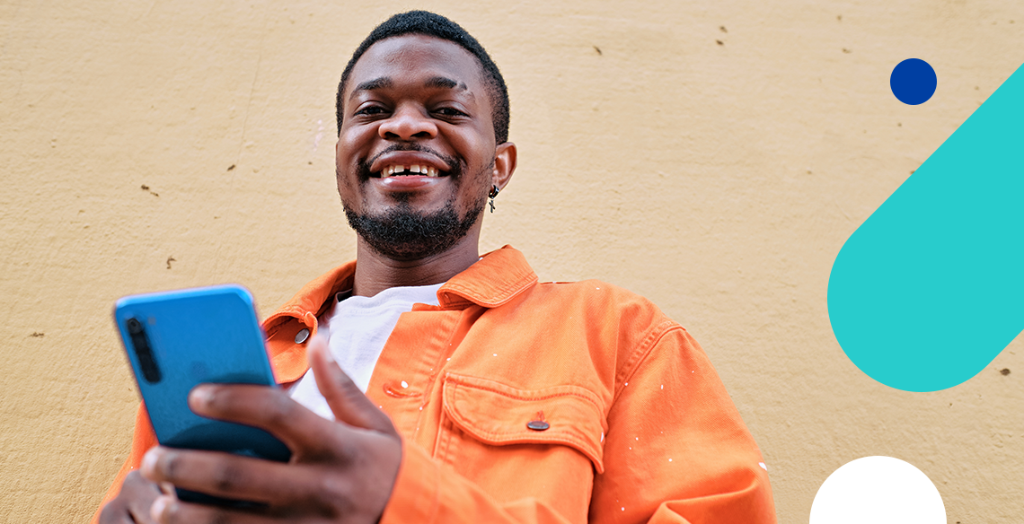 um homem negro de jaqueta laranja sorrindo e usando o celular para vender na shopee
